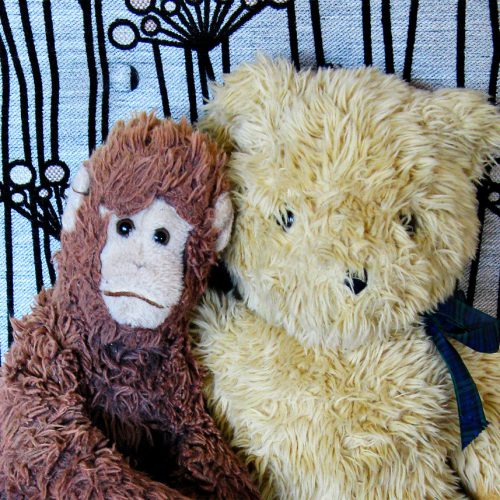 Two soft toys, a bear and a monkey, on an armchair upholstered in gorgeous Warwick fabric