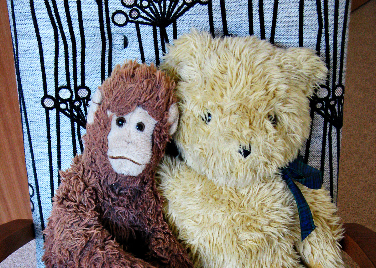 Two soft toys, a bear and a monkey, on an armchair upholstered in gorgeous Warwick fabric
