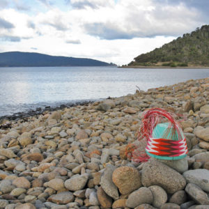 Telephone-wire basket, with chevron pattern, on the pebble beach at Cockle Bay Lagoon. Maria Island is in the background.