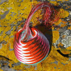 Pink, orange, brown and white wire basket in progress on a grey rock covered in bright orange-yellow lichen.