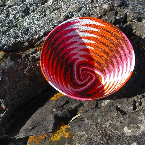 Finished chevron-patterned telephone-wire basket on lichen-covered coastal rocks at Penneshaw, Kangaroo Island.
