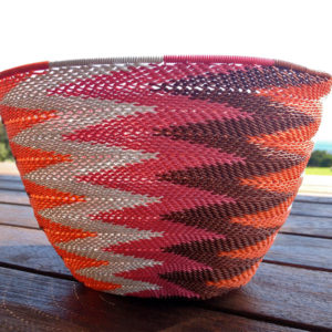 Close up of the chevron pattern of a telephone wire basket, with a paddock and azure sea in the background