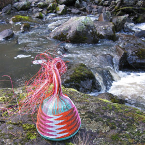 Chevron-patterned wire basket on lichen and moss covered rocks alongside a creek at Lemont, Tasmania.