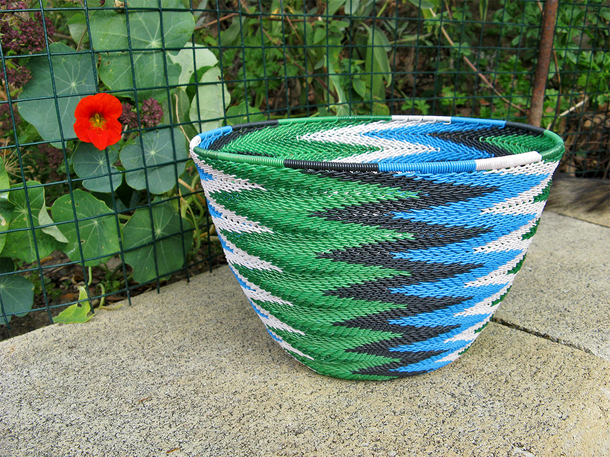 A completed telephone wire basket in a chevron pattern of blue, black, white and metallic green wires.