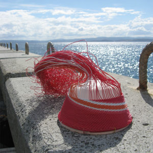 wire basket in progress on the concrete wall of the Maria Island jetty, with the glistening sea and a cloudy summer sky in the background.