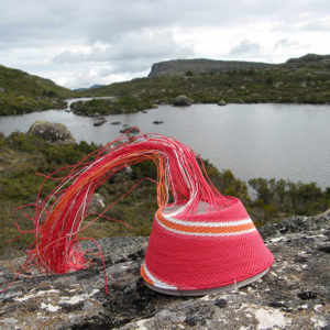 Red, pink, white and orange wire basket on a rock, with view of Long Tarns (Central Plateau, Tasmania) in the background