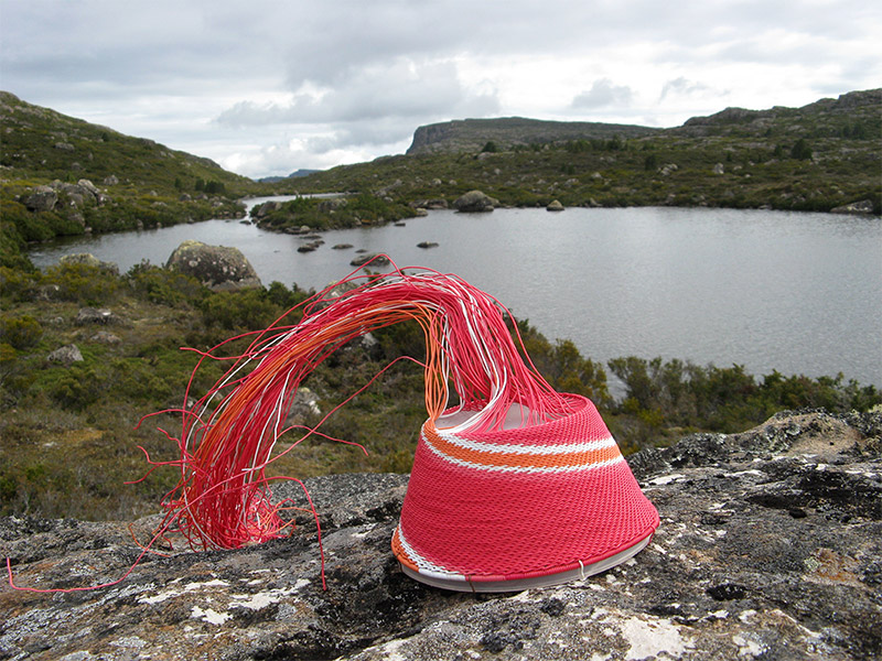 Red, pink, white and orange wire basket on a rock, with view of Long Tarns (Central Plateau, Tasmania) in the background