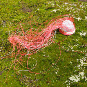 Pink, red, orange and white wire basket in progress, against bright green alpine vegetation on Mt Eliza, Tasmania