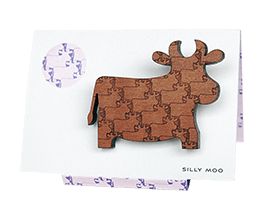 Cow brooch in Tasmanian Myrtle wood with a delicately engraved pattern of overlapping cows, on an easel-style card in a matching purple and white pattern