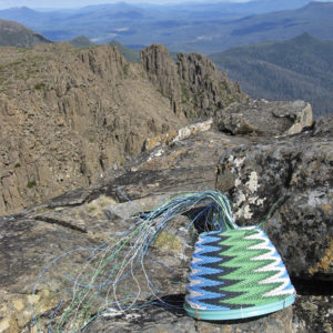 Wire basket in progress placed on lichen covered rocks with the mountains of Tasmania's south-west in the background.