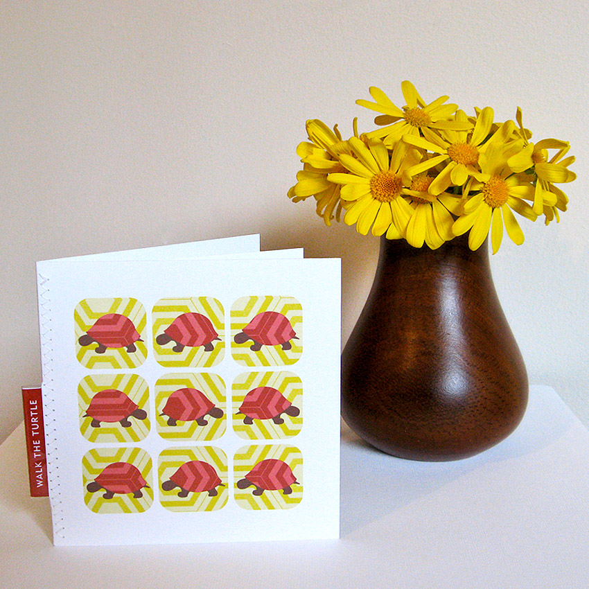 Walk the Turtle greeting card Walk the Turtle greeting card standing in front of a dark brown wooden vase with deep yellow daisies