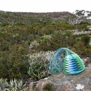 Telephone-wire basket on lichen-covered rocks with the top of Mt Wellington, from the South, in the background.